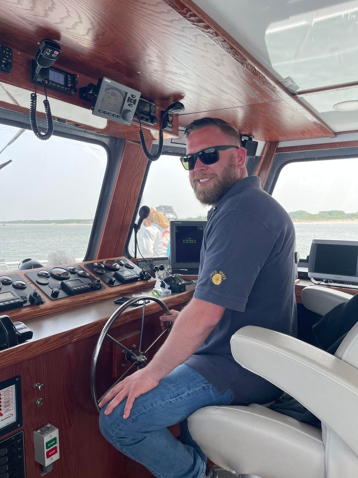 Man wearing sunglasses steering a boat in a cabin with wooden paneling.
