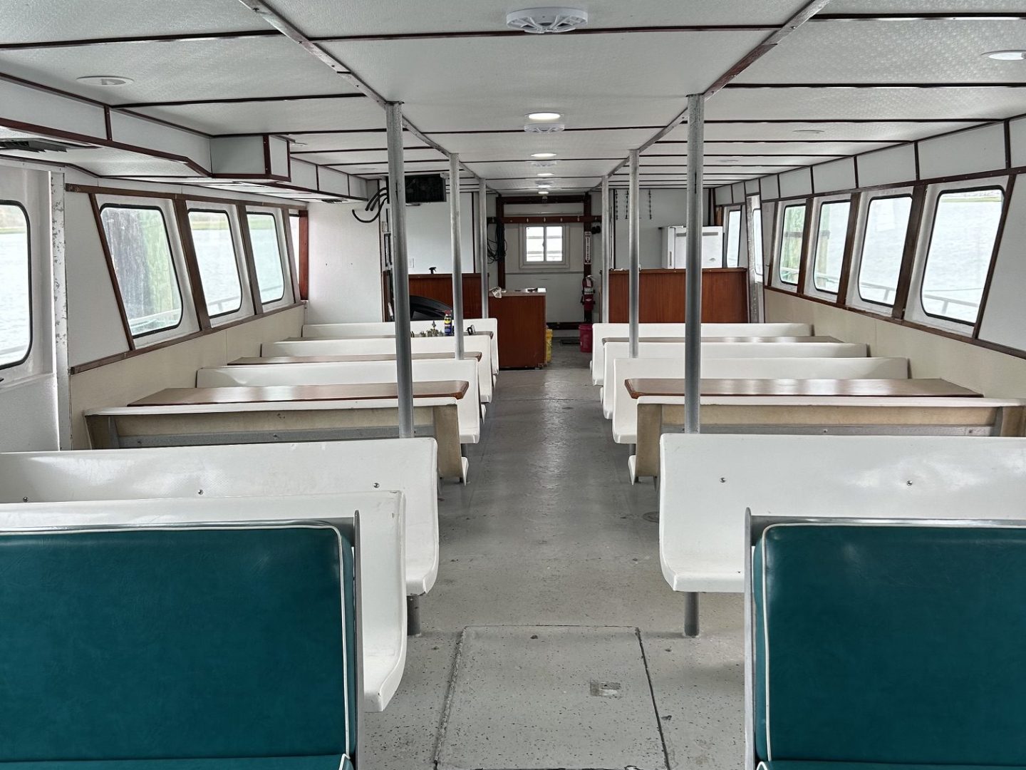 Empty boat interior with green seats and white walls, facing windows.