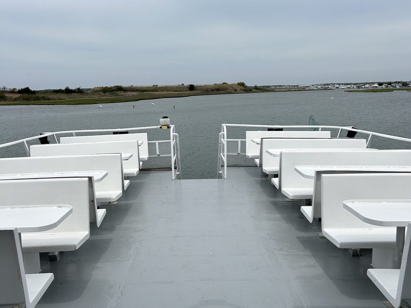 Empty ferry deck with white benches facing forward on a cloudy day.