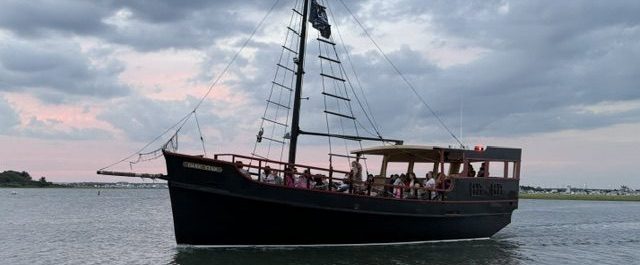 Sailboat with passengers on a calm water body at dusk.