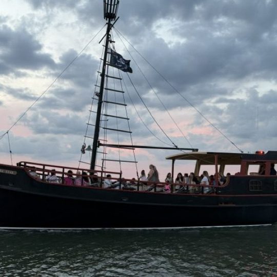 Inverted image of a boat with masts against a cloudy sky and water.