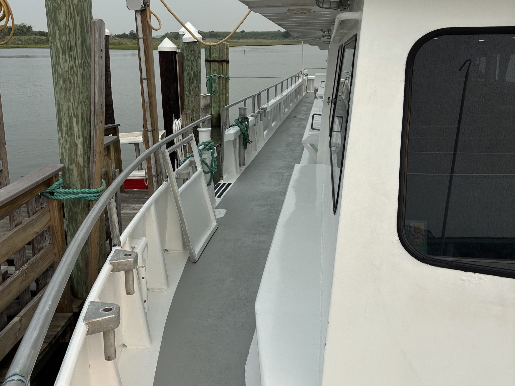 Side view of a moored white boat with railing, dock, and pilings.