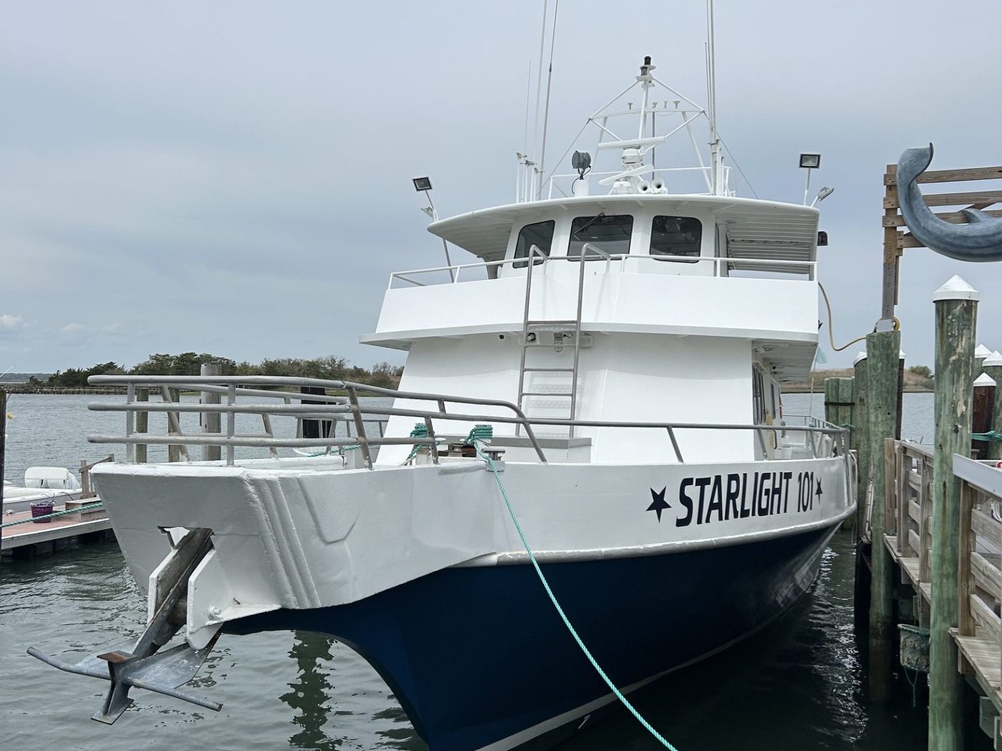 Docked boat named 'Starlight', blue and white, with calm water and cloudy sky.