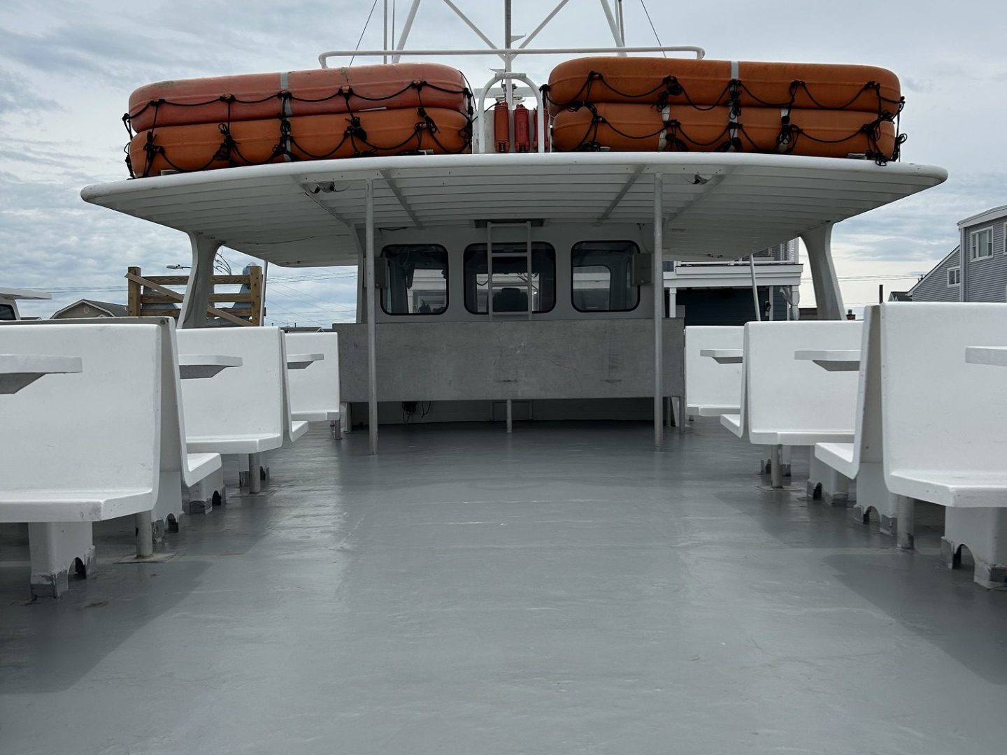 Deck of a boat with orange lifeboats on the roof and white benches.